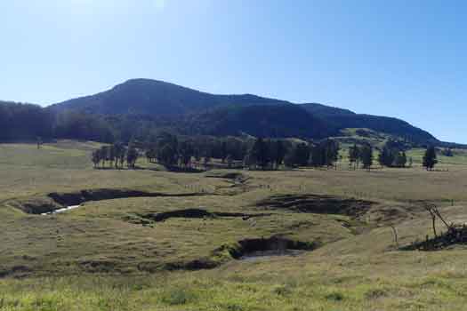 Looking over farmland with a stream towards a large rounded and forested mountain