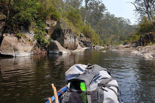 Inflatable kayak on a gentle river surrounded by trees on a cliff.