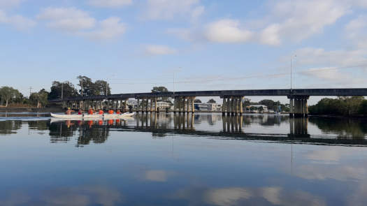 six paddlers on a river by a bridge